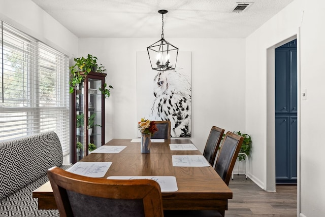 dining area featuring dark wood-type flooring, a textured ceiling, and a notable chandelier