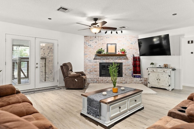 living room featuring french doors, a brick fireplace, a textured ceiling, ceiling fan, and light hardwood / wood-style floors