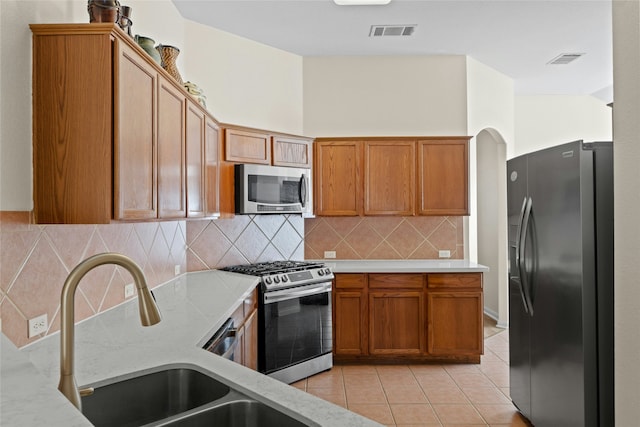 kitchen with appliances with stainless steel finishes, decorative backsplash, sink, light stone counters, and light tile patterned floors