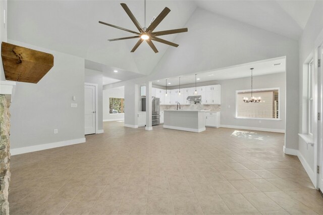 unfurnished living room featuring ceiling fan with notable chandelier, light tile patterned floors, and high vaulted ceiling