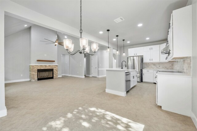 kitchen featuring a kitchen island with sink, a stone fireplace, hanging light fixtures, appliances with stainless steel finishes, and white cabinetry