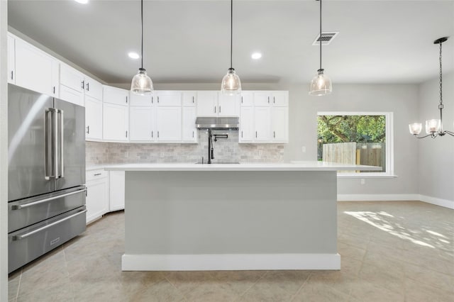 kitchen with high end refrigerator, hanging light fixtures, and a kitchen island with sink