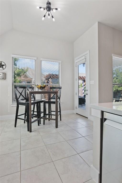 tiled dining space with a healthy amount of sunlight, vaulted ceiling, and an inviting chandelier