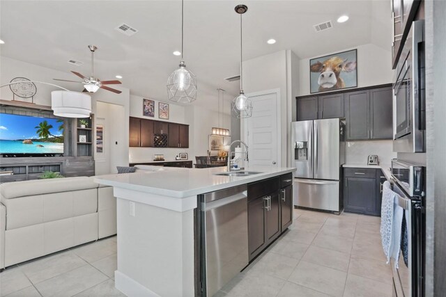 kitchen featuring dark brown cabinets, stainless steel appliances, sink, light tile patterned floors, and a center island with sink