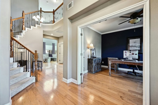 entryway with wood-type flooring, ceiling fan with notable chandelier, and ornamental molding