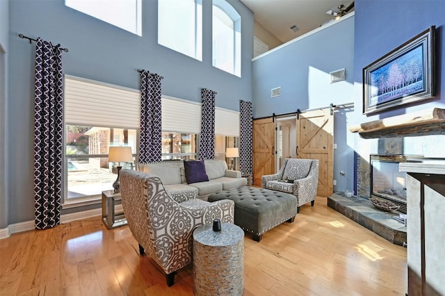 living room with a barn door, light hardwood / wood-style floors, and a high ceiling