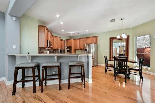 kitchen with kitchen peninsula, appliances with stainless steel finishes, light wood-type flooring, a kitchen bar, and a chandelier