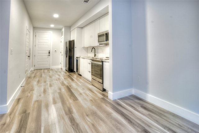 kitchen featuring white cabinetry, sink, stainless steel appliances, light hardwood / wood-style floors, and decorative backsplash