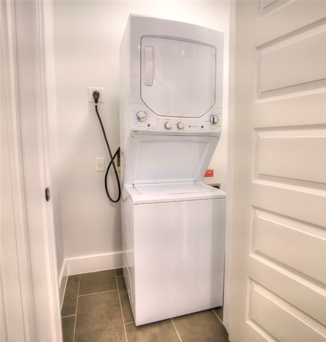 laundry area with dark tile patterned floors and stacked washer / drying machine