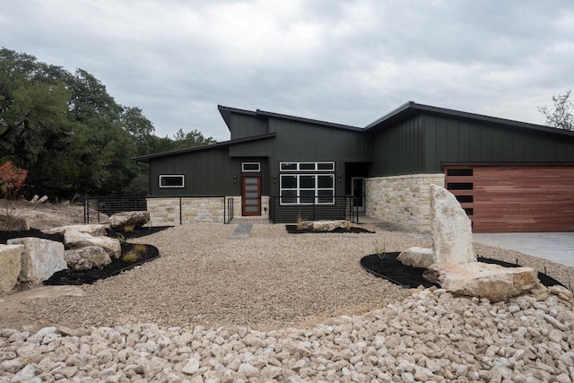 view of front of home with a garage, stone siding, and fence