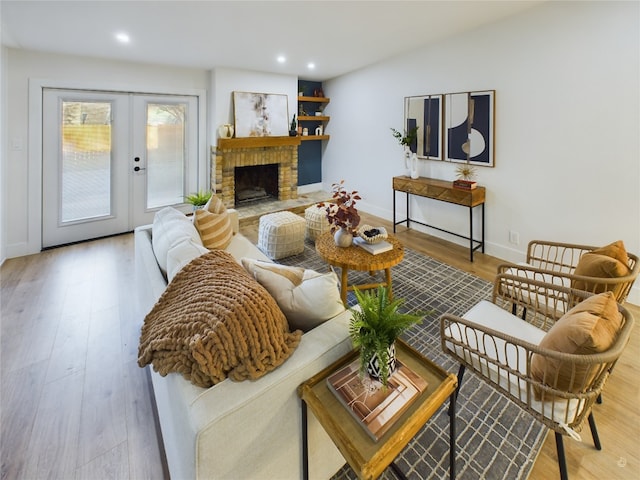 living room featuring vaulted ceiling, a fireplace, light hardwood / wood-style flooring, and french doors