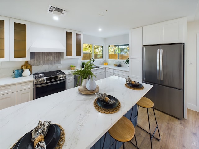 kitchen with white cabinetry, a breakfast bar, light hardwood / wood-style floors, and appliances with stainless steel finishes