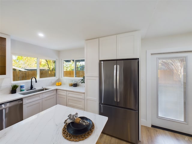 kitchen with appliances with stainless steel finishes, light stone counters, sink, white cabinets, and light hardwood / wood-style floors