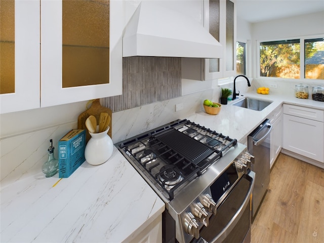 kitchen featuring custom range hood, stainless steel appliances, sink, white cabinets, and light hardwood / wood-style floors