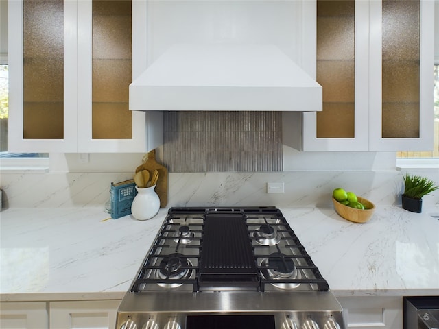 kitchen featuring backsplash, white cabinetry, stainless steel stove, and custom range hood