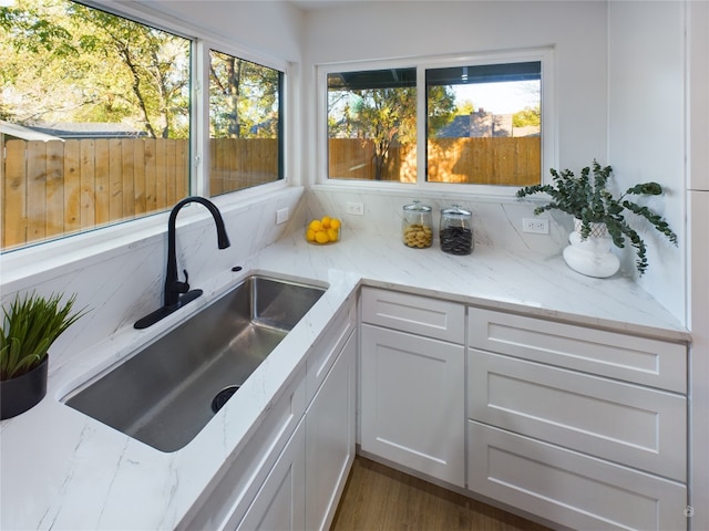 kitchen featuring light stone countertops, plenty of natural light, white cabinets, and sink