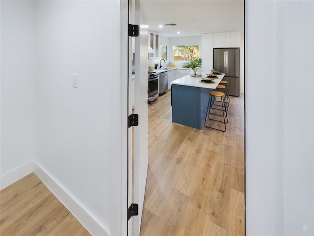 kitchen with a kitchen bar, appliances with stainless steel finishes, a kitchen island, light hardwood / wood-style floors, and white cabinetry