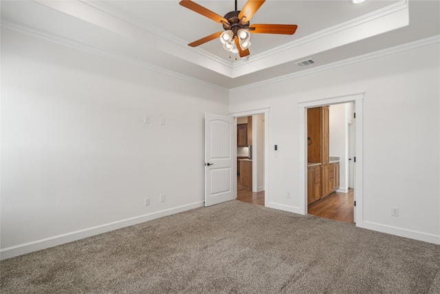 unfurnished bedroom with ceiling fan, dark carpet, crown molding, and a tray ceiling