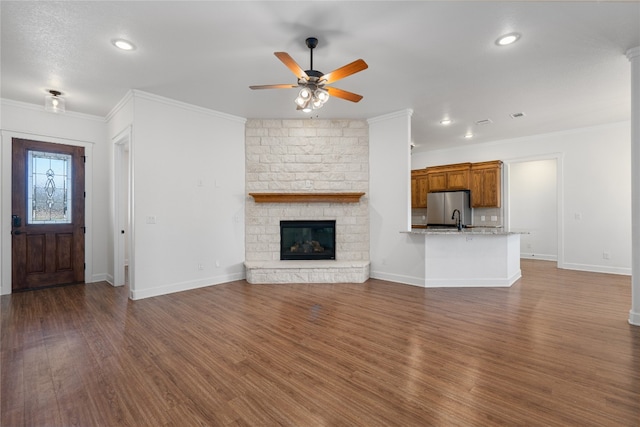 unfurnished living room with ceiling fan, a stone fireplace, dark hardwood / wood-style flooring, and ornamental molding