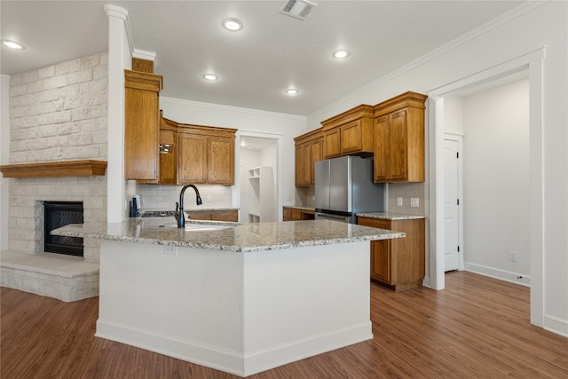 kitchen featuring decorative backsplash, light stone counters, sink, hardwood / wood-style flooring, and stainless steel refrigerator