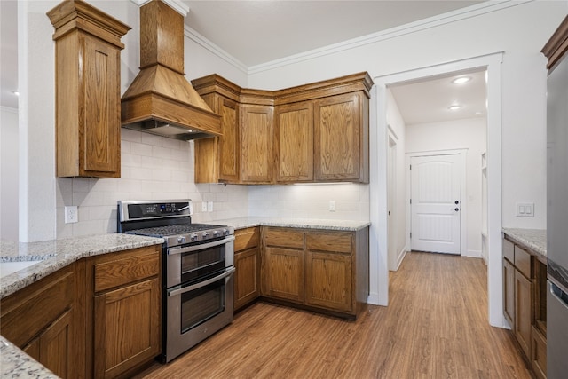 kitchen featuring light stone counters, custom range hood, crown molding, light hardwood / wood-style flooring, and double oven range