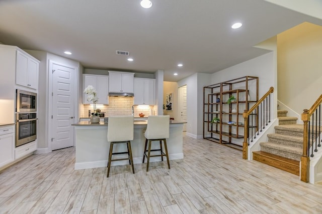 kitchen with a breakfast bar area, white cabinetry, light hardwood / wood-style flooring, and a kitchen island