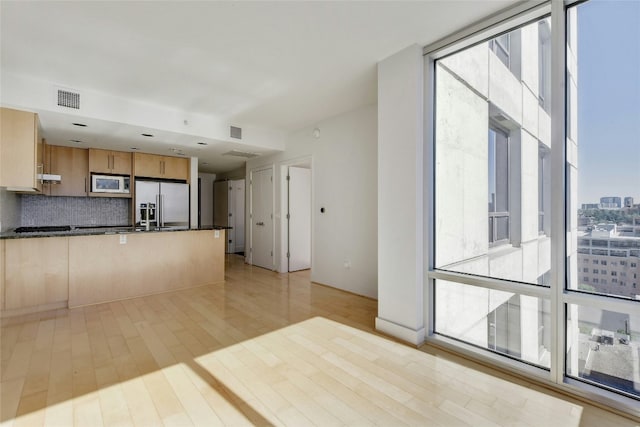 kitchen with stainless steel fridge, light hardwood / wood-style flooring, white microwave, and a healthy amount of sunlight