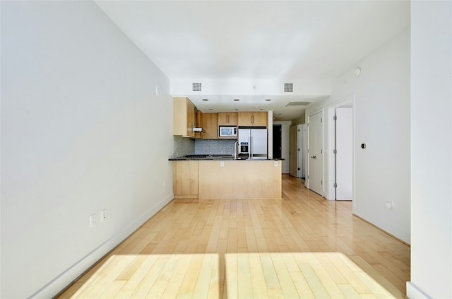 kitchen featuring stainless steel microwave, white fridge with ice dispenser, tasteful backsplash, light hardwood / wood-style flooring, and kitchen peninsula