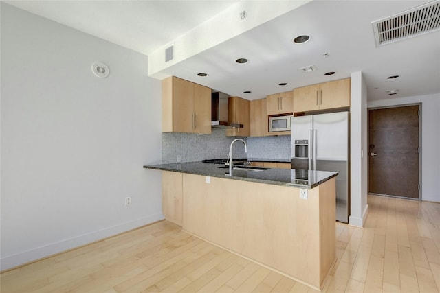 kitchen with wall chimney exhaust hood, dark stone countertops, and kitchen peninsula