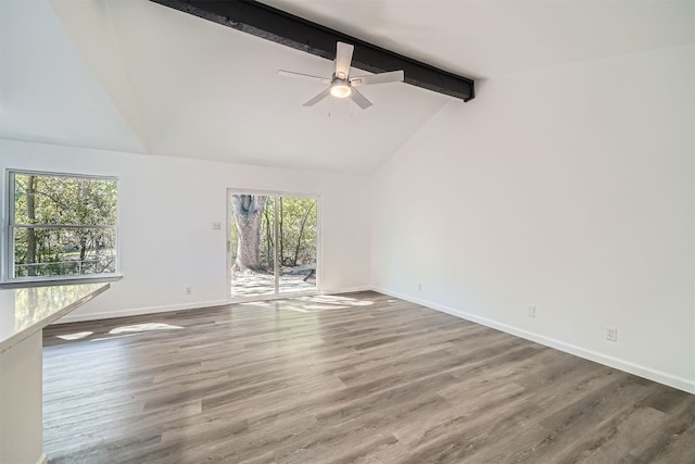 unfurnished living room featuring beamed ceiling, wood-type flooring, and a wealth of natural light