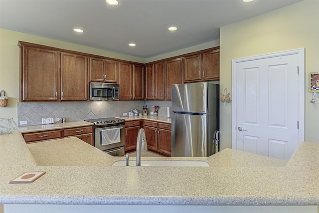 kitchen featuring kitchen peninsula, light stone countertops, backsplash, stainless steel appliances, and sink