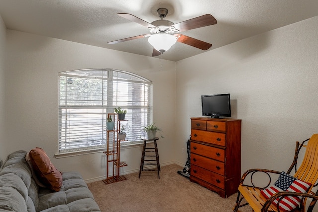 living area with ceiling fan, light colored carpet, and a textured ceiling