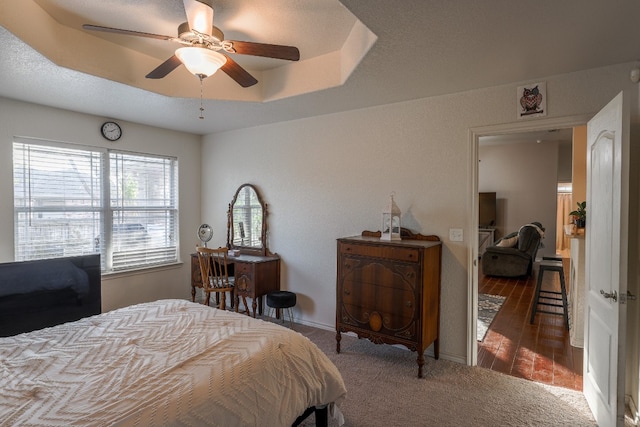 carpeted bedroom with ceiling fan and a raised ceiling