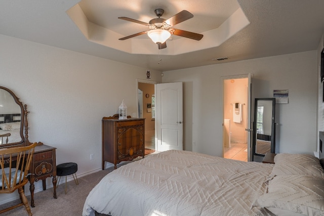 bedroom with ceiling fan, light colored carpet, ensuite bathroom, and a tray ceiling