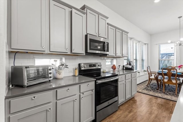 kitchen with appliances with stainless steel finishes, gray cabinetry, dark wood-style floors, backsplash, and dark countertops