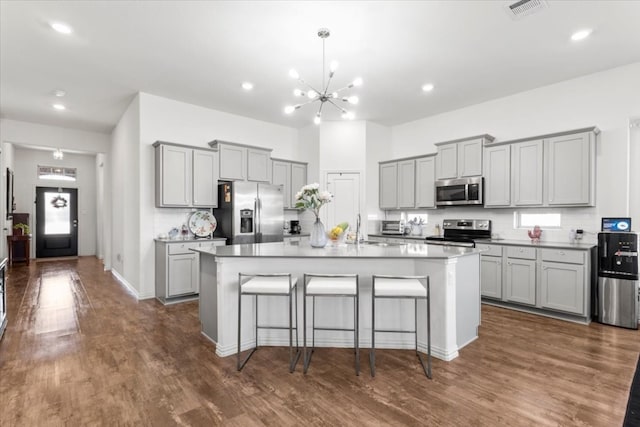 kitchen with a kitchen bar, gray cabinets, an island with sink, and appliances with stainless steel finishes