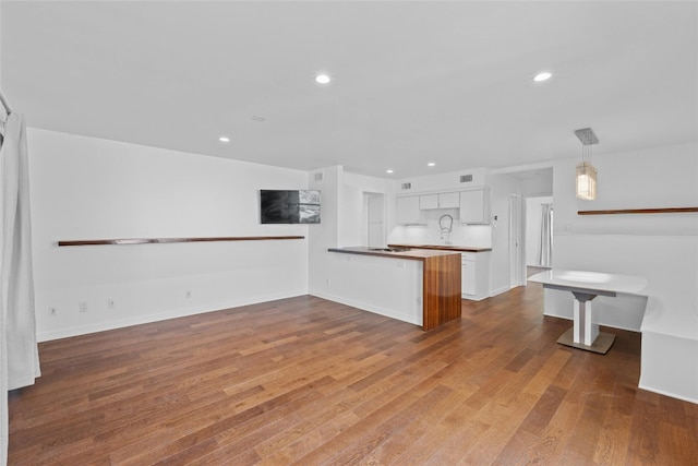 kitchen with kitchen peninsula, light hardwood / wood-style floors, white cabinetry, and hanging light fixtures