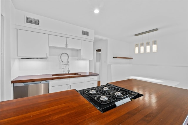 kitchen with stainless steel dishwasher, sink, white cabinets, butcher block countertops, and hanging light fixtures