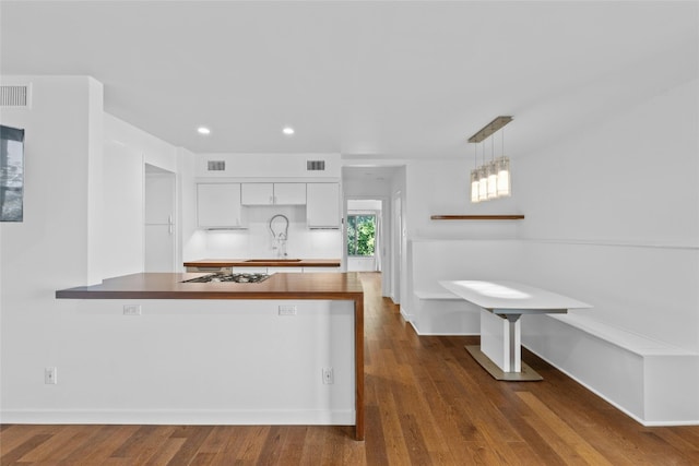 kitchen featuring gas stovetop, dark wood-type flooring, pendant lighting, white cabinets, and butcher block counters