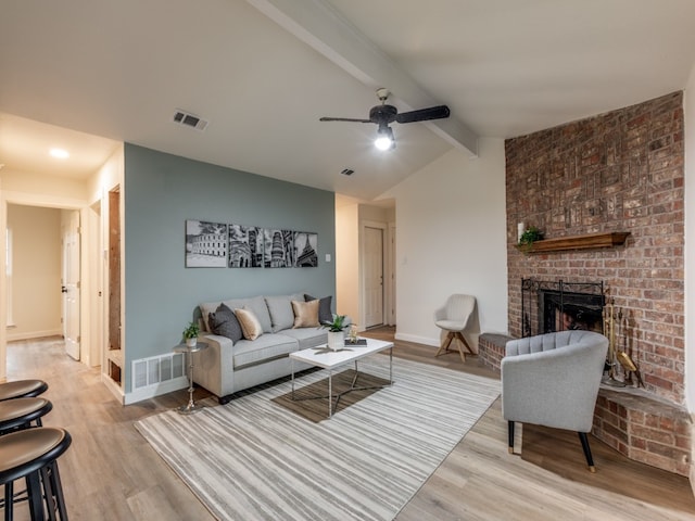 living room featuring lofted ceiling with beams, ceiling fan, light hardwood / wood-style floors, and a brick fireplace