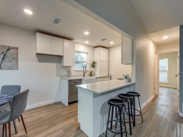 kitchen with dishwasher, a kitchen bar, light hardwood / wood-style flooring, and white cabinetry