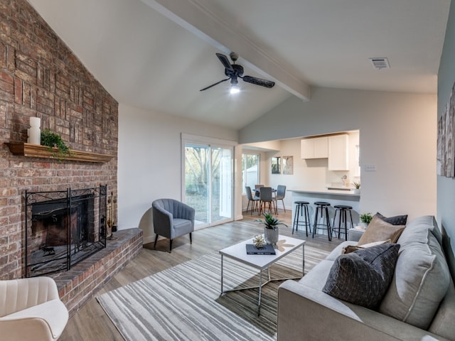 living room with vaulted ceiling with beams, light wood-type flooring, a brick fireplace, and ceiling fan