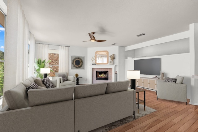 living room with light hardwood / wood-style flooring, a tile fireplace, and ceiling fan