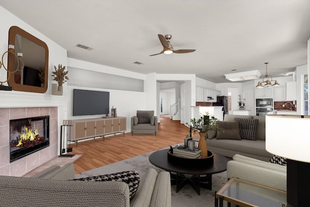 living room featuring ceiling fan, a tiled fireplace, sink, and light hardwood / wood-style flooring