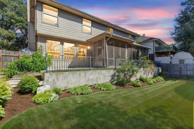 back house at dusk with a lawn and a sunroom