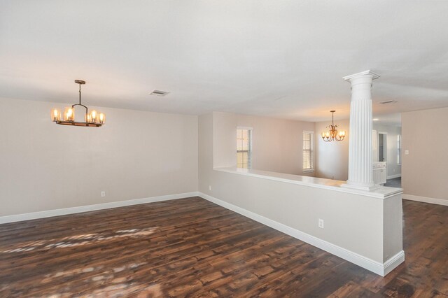 empty room featuring decorative columns, dark hardwood / wood-style flooring, and a chandelier