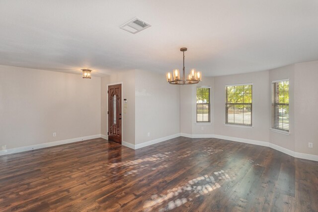 spare room with a chandelier and dark wood-type flooring