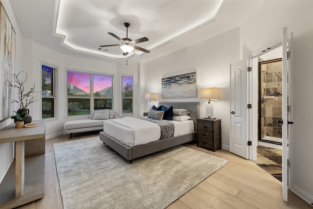 bedroom with light wood-type flooring, a raised ceiling, and ceiling fan