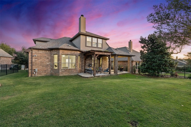 back house at dusk featuring a lawn and a patio