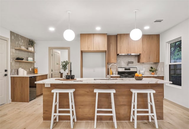 kitchen with pendant lighting, a kitchen island with sink, and stainless steel stove